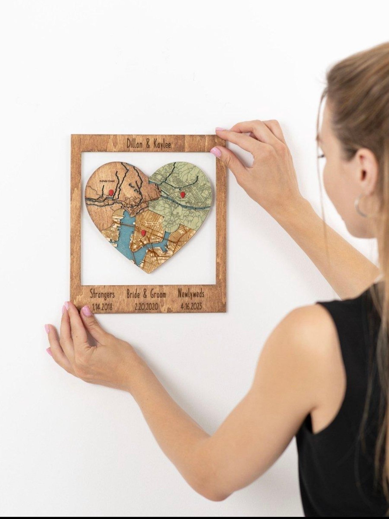 A woman hanging a heart-shaped wooden anniversary map on her wall